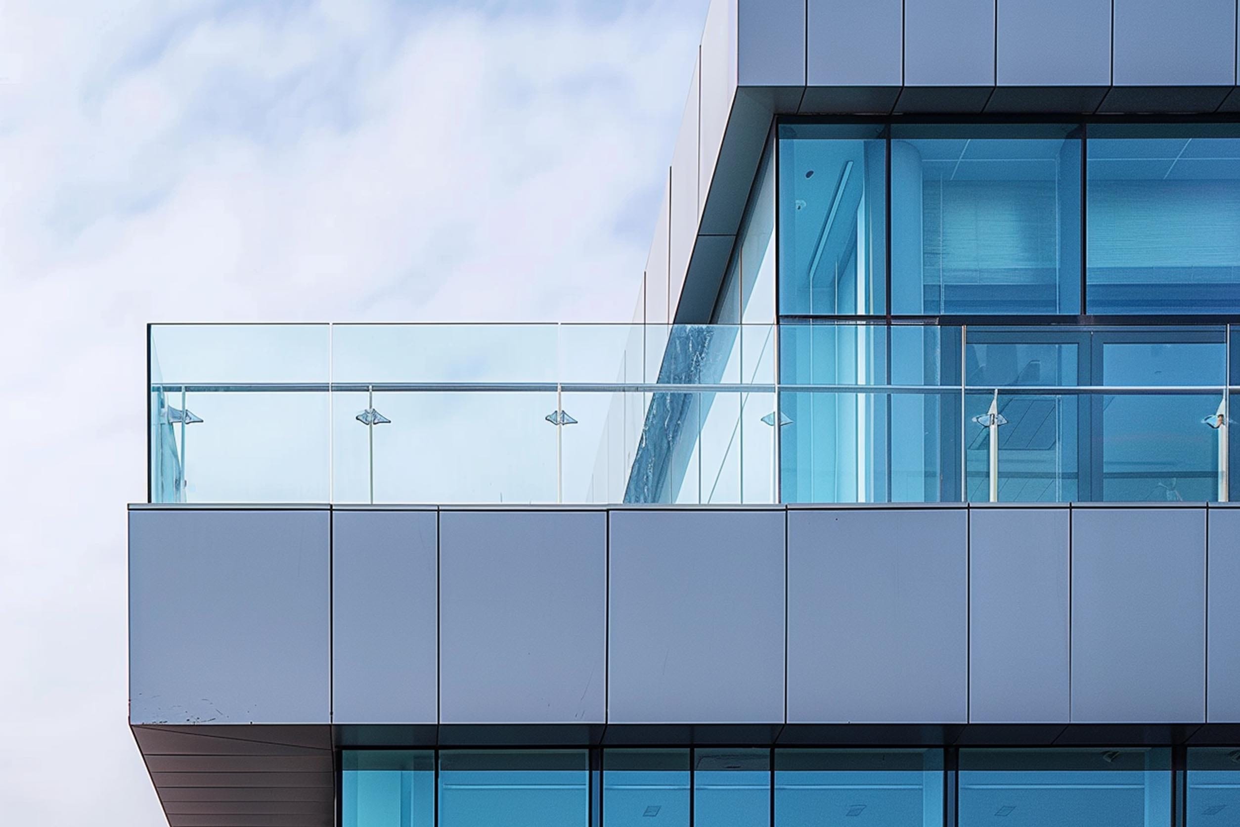 Exterior corner of a modern building with blue-tinted glass windows and a balcony with glass railings